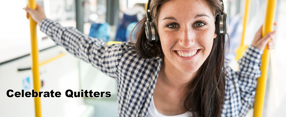 Young woman in headphones, smiling confidently on a bus. She's casually dressed in a checked shirt. Text reads Celebrate Quitters, conveying a positive message.