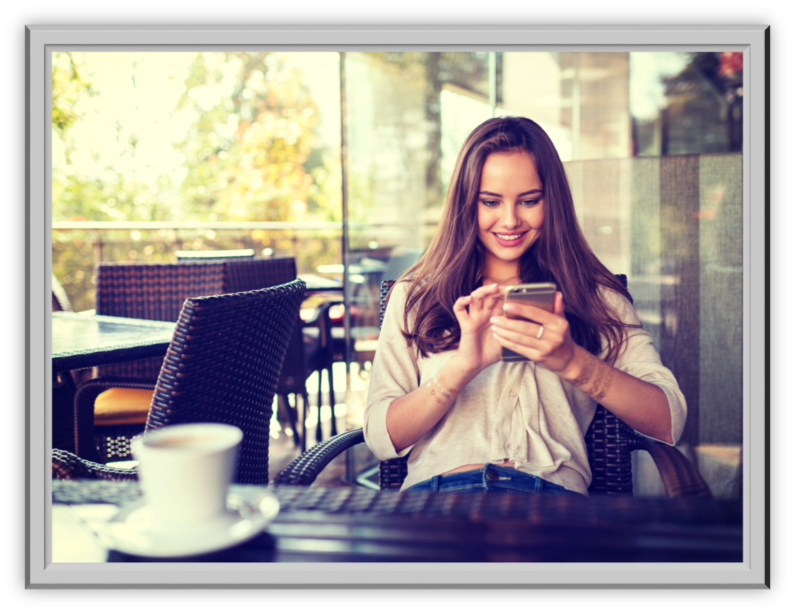 Smiling woman using a smartphone at an outdoor café, sitting on a wicker chair. A cup of coffee is on the table, with a sunny background visible.