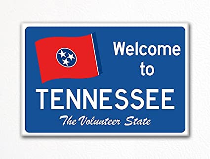 Blue sign reads 'Welcome to Tennessee, The Volunteer State' with a red flag featuring three white stars in a blue circle, evoking a welcoming tone.