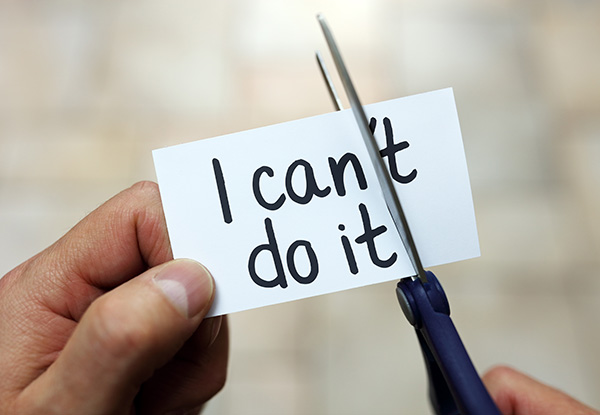 A hand cuts a paper reading: I can't do it with scissors, removing can't to change the message to I can do it, symbolizing overcoming self-doubt.